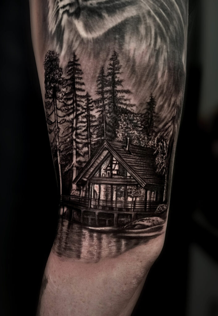 Black and grey cabin and forest landscape tattoo on arm